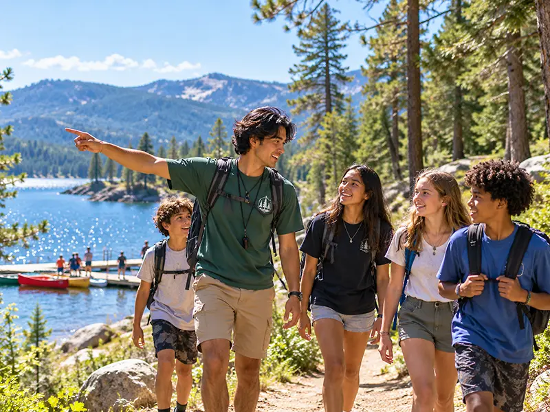 Summer camp counselor leading a group of campers along a lakeside trail